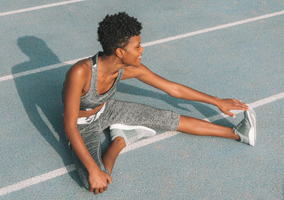 High angle view of smiling woman stretching leg on sports track