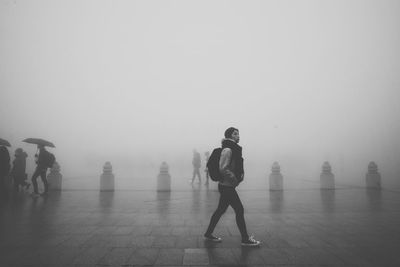 Full length on woman walking at pedestrian zone against sky during foggy weather