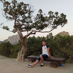 Full length portrait of man sitting on tree