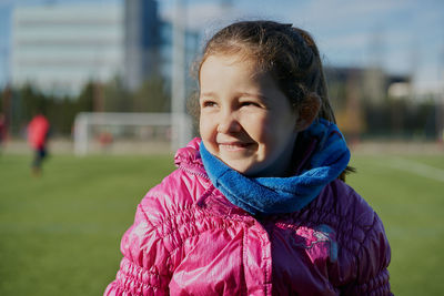 Smiling little girl wearing a pink coat in a football stadium