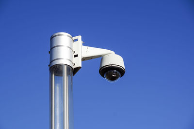 Low angle view of security camera on pole against clear blue sky