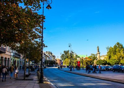 People walking on street in city against blue sky