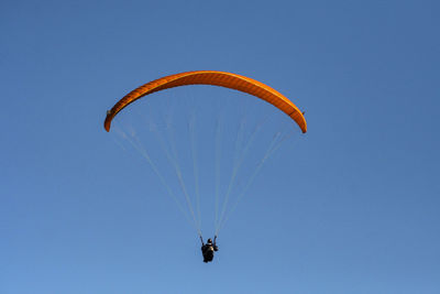 Low angle view of person paragliding against clear blue sky