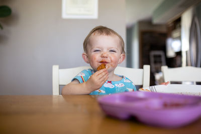 Portrait of baby girl eating food while sitting by table at home