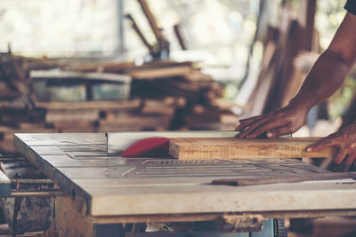 Cropped hands of carpenter holding wooden plank on table in workshop