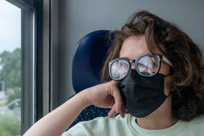View of young woman traveling by train during pandemic wearing glasses and black mask.