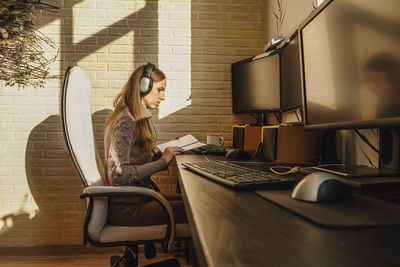 Woman reading book by computer on table