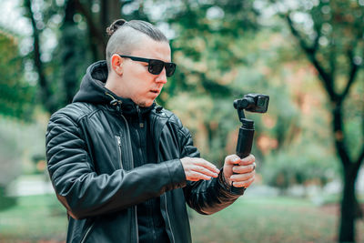 Midsection of man holding sunglasses standing against trees