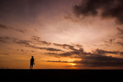 Silhouette woman standing at beach against sky during sunset