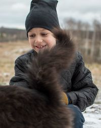 Portrait of smiling boy, laying with cat on snow land