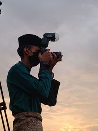 Low angle view of man holding camera against sky