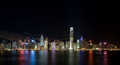 Illuminated cityscape at victoria harbour against sky at night