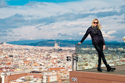 Young woman wearing warm clothing while standing on balcony against cityscape