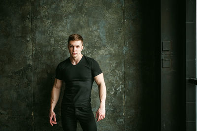 Portrait of muscular man standing by wall