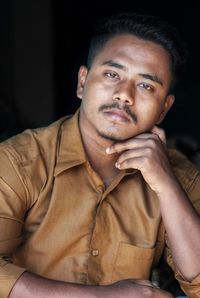 Portrait of young man sitting against black background