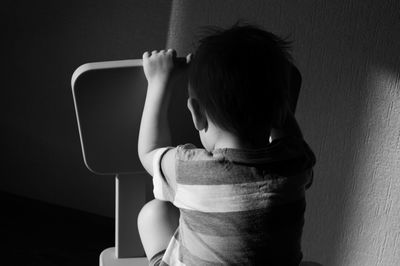 Rear view of boy sitting on wall at home