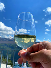 Close-up of hand holding glass against sky