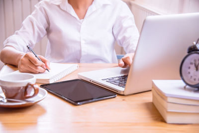 Midsection of woman using smart phone while sitting on table