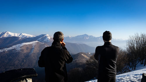 People standing on snowcapped mountain against clear sky