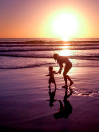 Mother and son walking on shore during sunset
