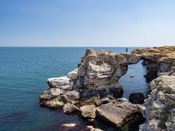 Rocks by sea against clear blue sky