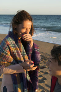 Mother with smart phone and son against sea and sky during sunset