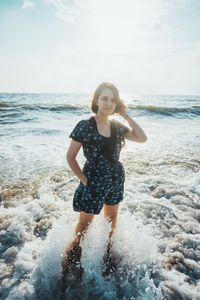 Beautiful young woman standing at seashore against sky