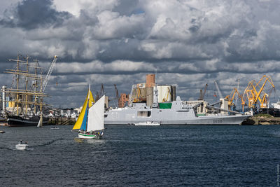 Ships in sea at commercial dock against cloudy sky