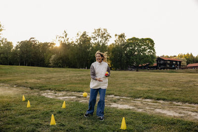 Happy female counselor holding balls while standing amidst sports cones in playground