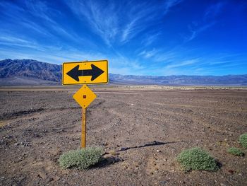 Arrow sign on road against sky