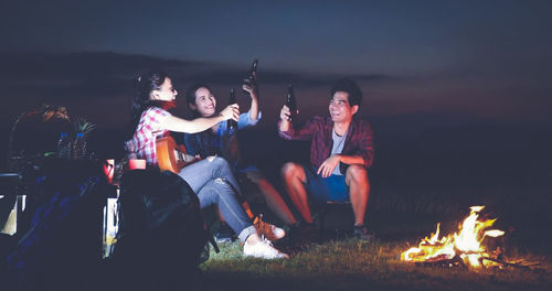 People sitting on bonfire against sky at night