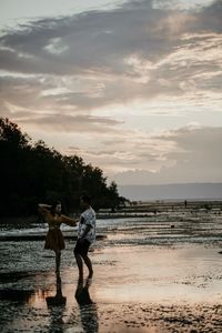 Men standing on beach against sky during sunset