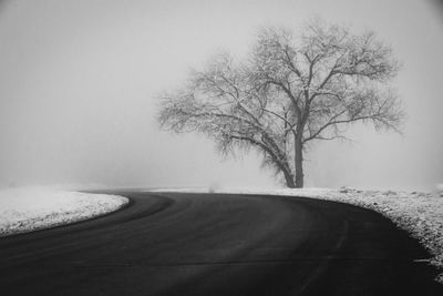 Road amidst bare trees against sky during winter