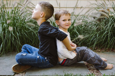 Two happy small boys sit back to back in yard