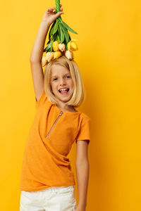 Portrait of girl holding tulip flowers on head against yellow background