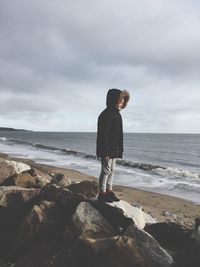 Boy standing on rock by sea against sky