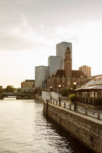 Buildings by river against sky in city during sunset