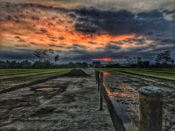 Road amidst field against sky during sunset