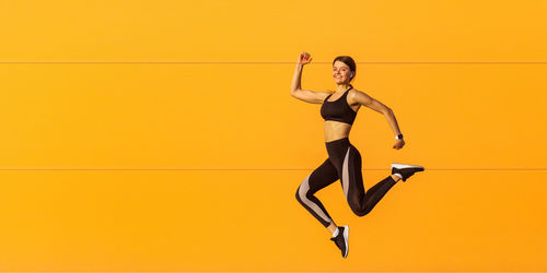 Full length of man jumping against yellow background