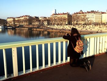 Rear view of woman kneeling by railing over river in city