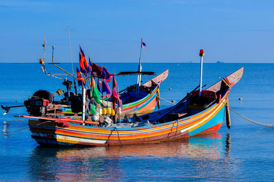 Fishing boats moored in sea against blue sky