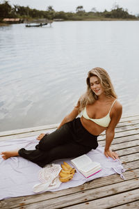 Portrait of young woman sitting on pier over lake