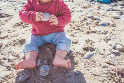 Low section of cute girl sitting on sand at beach