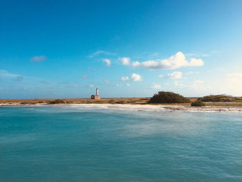 Lighthouse on grass by sea against sky