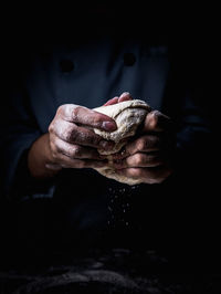 Midsection of man kneading dough in darkroom