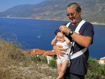 Smiling man holding baby girl while standing against sea