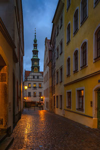 Illuminated street amidst buildings in city at dusk