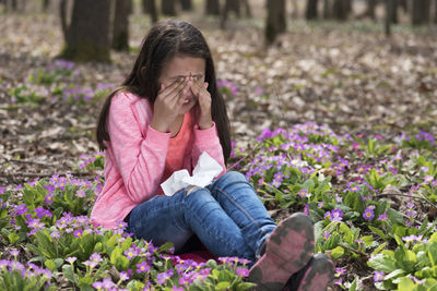 Girl sneezing while sitting on flowering plants