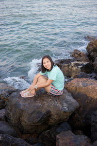 Portrait of young woman sitting on rock by sea