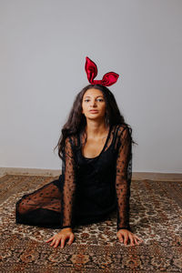 Portrait of a young woman sitting against wall